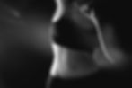 Black and white image of a woman in a sports bra, mid-motion, with dynamic blur effect. Dark background, emphasizing movement and form.