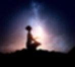 Silhouette of a person meditating with a glowing tablet under a starry night sky, evoking tranquility and wonder against mountain outlines.