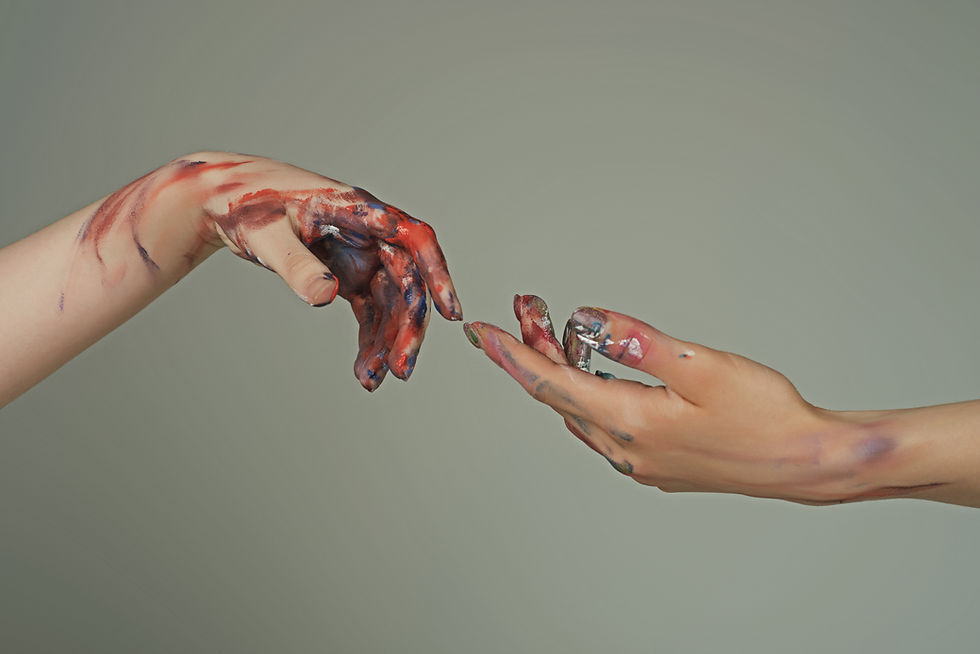 Two hands covered in colorful paint reaching towards each other against a gray background, suggesting creativity and connection.