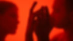 Silhouettes of two faces and intertwined hands against a vibrant red background, creating an intimate and dramatic atmosphere.