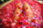 Legs submerged in a bathtub filled with vibrant red, pink, and purple flower petals, creating a relaxing, colorful scene.