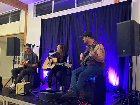 Three performers playing instruments (electric guitar, bass guitar, and bass guitar) and singing. 
