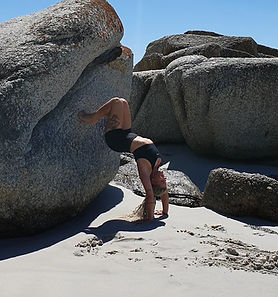 Phoenixx doing a backbend on a sandy beach with rocks