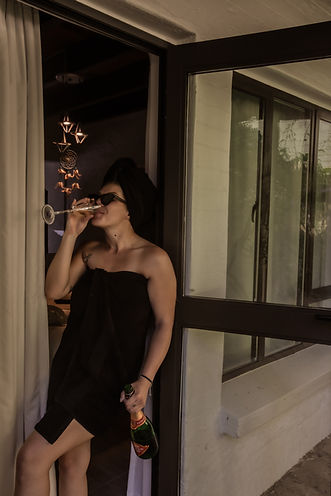 Woman in a black towel drinking wine by a balcony door