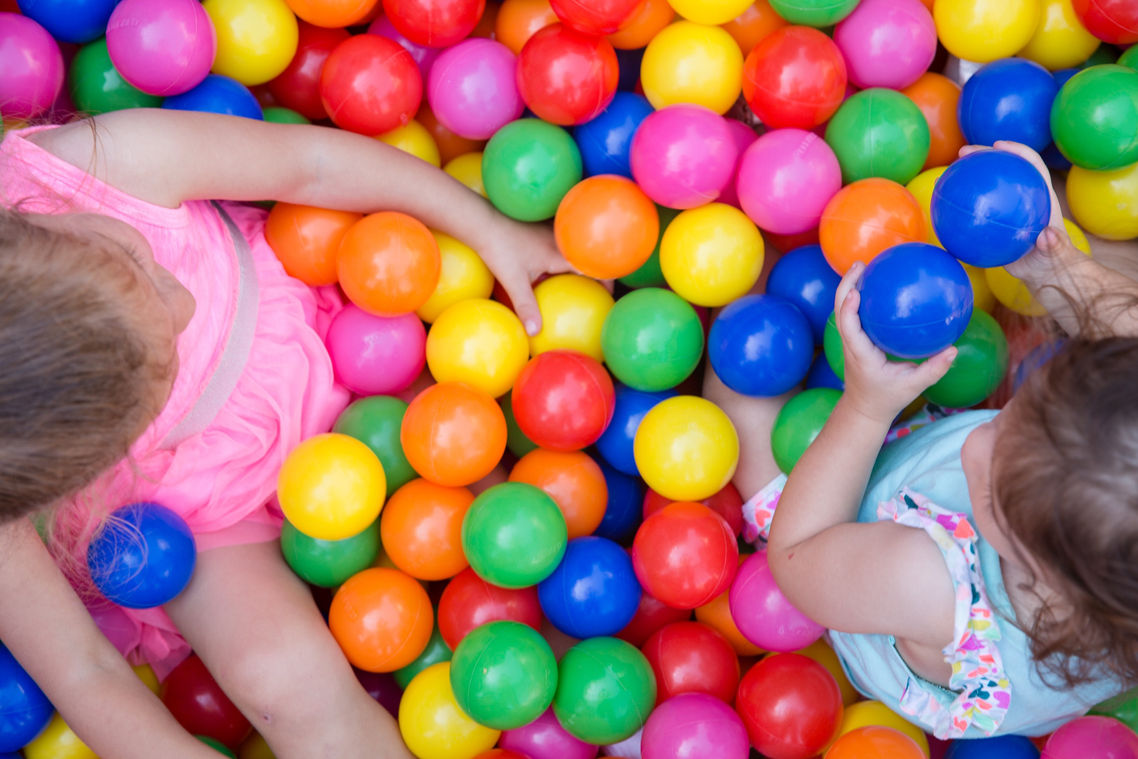 2 children playing in a colorful  ball pit.