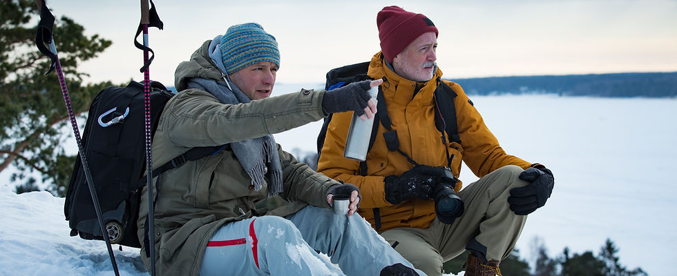 Two mature men exploring Finland in winter. Hikers sit on top of rock, take pictures with