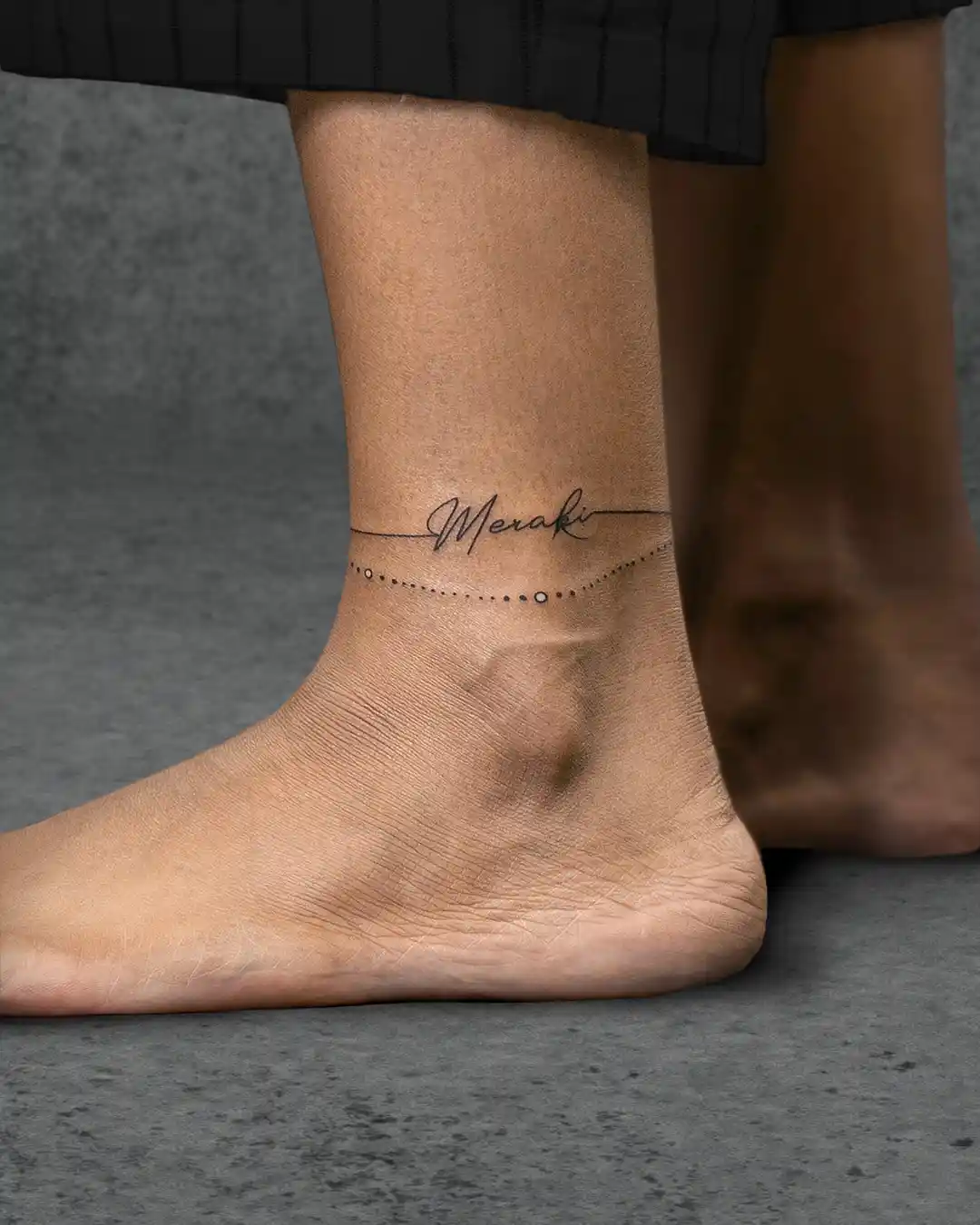Delicate "Meraki" tattoo on a woman's ankle, meaning to do something with soul, creativity, or love, symbolizing her passion.