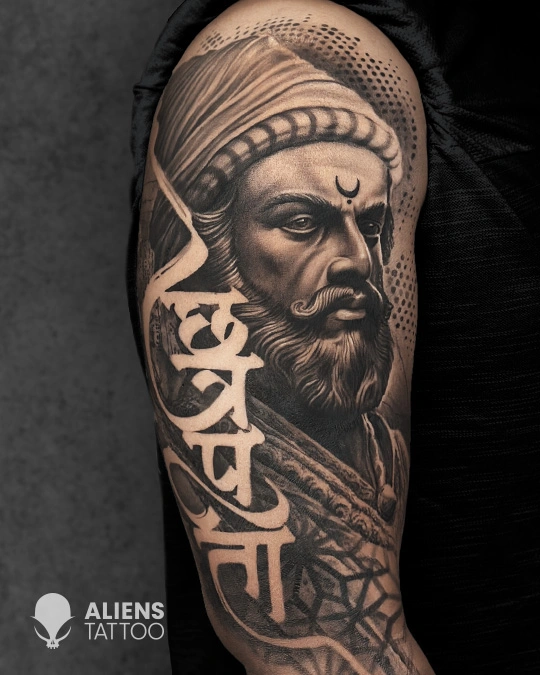 Hyper realistic black and grey Chhatrapati Shivaji Maharaj portrait tattoo with fierce expression and Devanagari script on the upper arm, created by Aliens Tattoo, the best tattoo studio in pune.