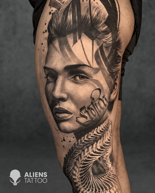 Realistic female portrait tattoo with stylized lettering and feather design on arm in black and grey