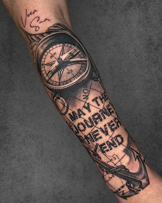 A travel-themed tattoo on a man’s forearm, featuring a compass and the quote "May the journey never end," symbolizing a lifelong adventure.