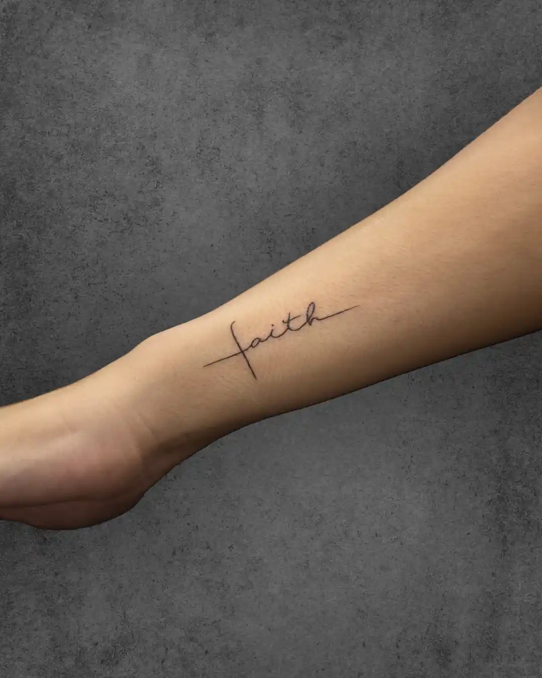 Simple "Faith" tattoo on a woman's forearm, with the word artistically integrated into a cross, reflecting personal belief and spirituality.