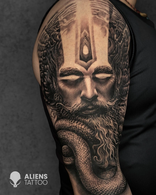 Realistic sadhu face tattoo with third eye and coiled snake on upper arm by Aliens Tattoo