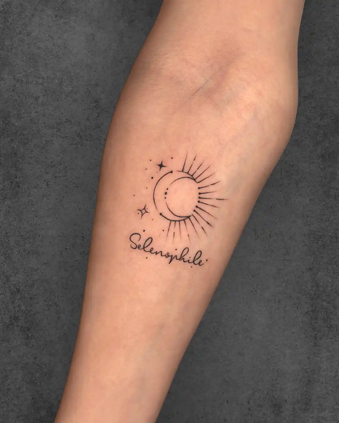 Small minimalist moon and sun tattoo on a woman's forearm with the word "Selenophile," symbolizing a love for the moon and celestial beauty.