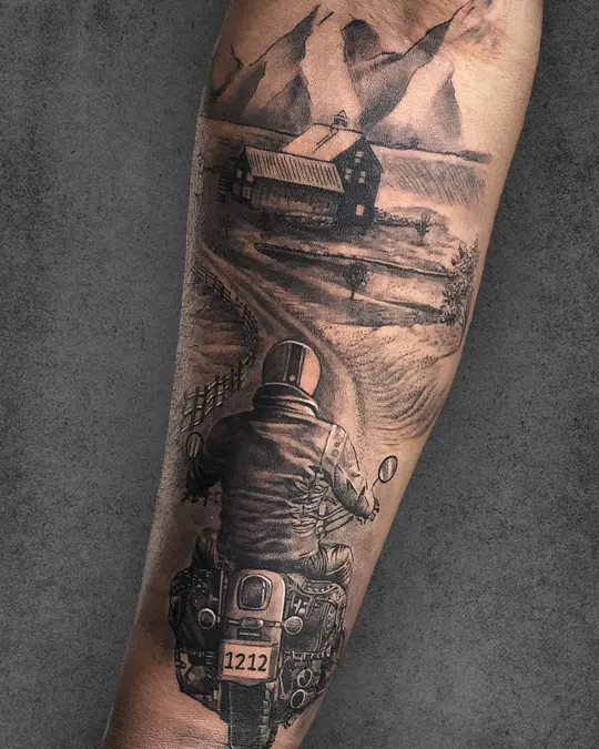 Realistic travel tattoo on a man’s forearm, showing a motorcyclist riding into the mountains, reflecting freedom and adventure.