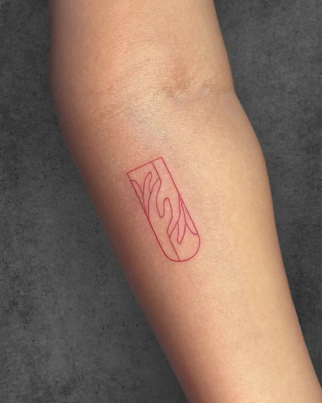 Minimalist flame tattoo on a woman’s forearm in a red ink outline, symbolizing passion, energy, and intensity.