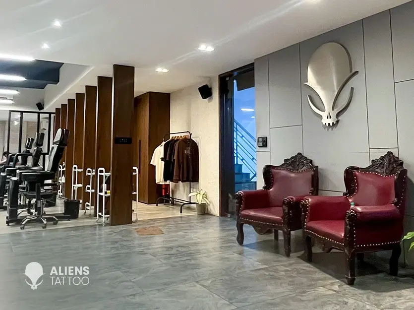 Interior of Aliens Tattoo studio in Bangalore featuring modern tattoo chairs, wooden partitions, merchandise rack, and luxury waiting area with red chairs and alien logo wall design