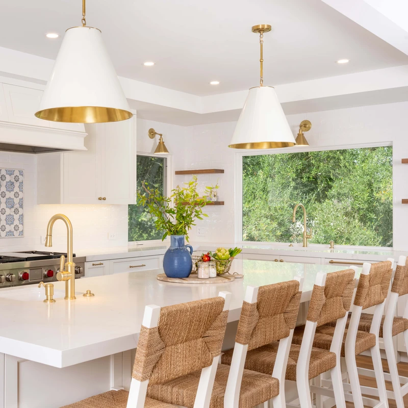 White kitchen island with woven-back stools, pendant lights and garden-facing windows.