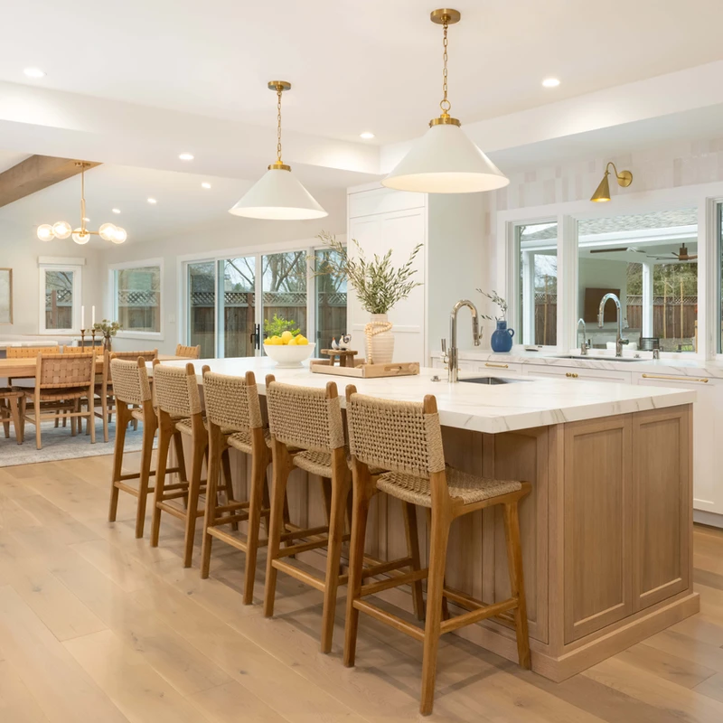 Kitchen island with woven-back stools and white pendants, opening to the dining area.