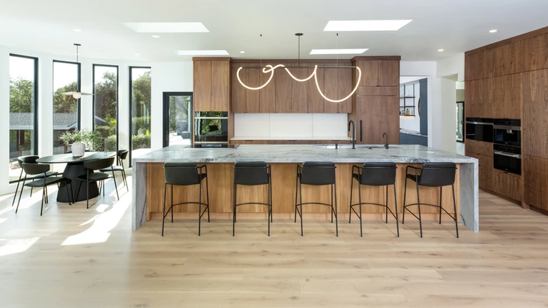Kitchen island with five stools, skylights and a dining area beside tall windows.