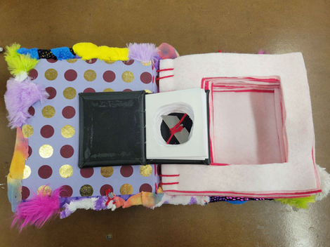 An open book with felt for pages with a smaller book laying on top that has been hollowed out and holds a razor blade inside. 