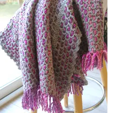 Plaid en crochet tissé gris avec des lignes horizontales roses et fuchsia, posé sur un fauteuil blanc dans un intérieur lumineux