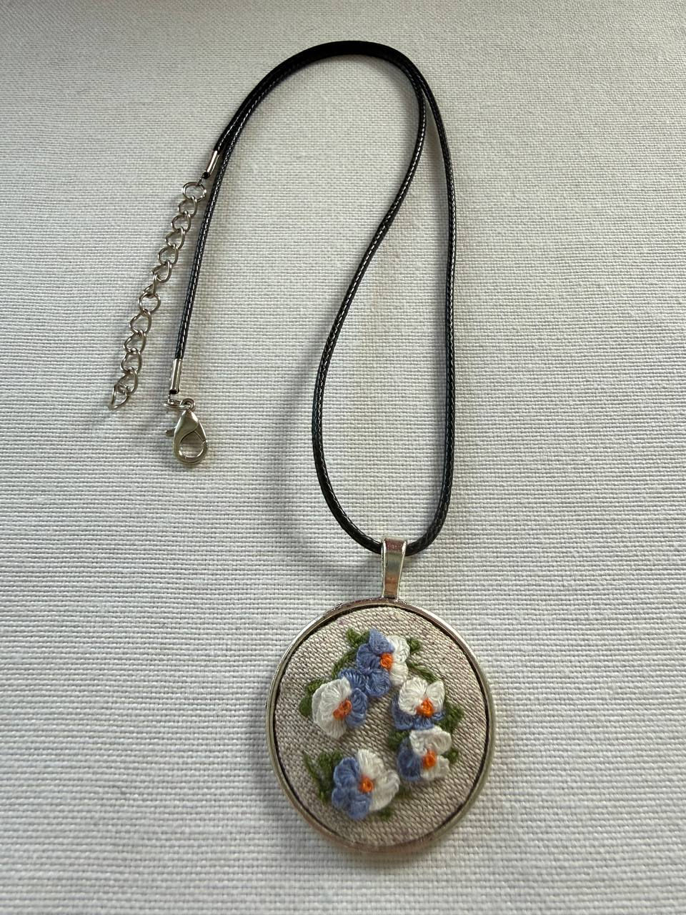 Thumbnail: Hand embroidered blue and white wildflower pendant on natural linen in a round silver-tone vintage style frame with a cord