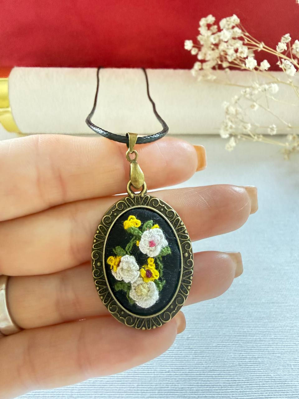 Hand embroidered white and yellow floral pendant on black linen in a vintage style oval frame. in a hand