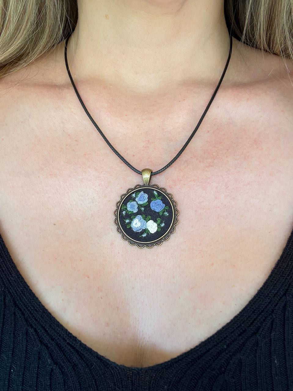 Hand embroidered blue and white rose pendant in a vintage style round frame with black waxed cord necklace worn