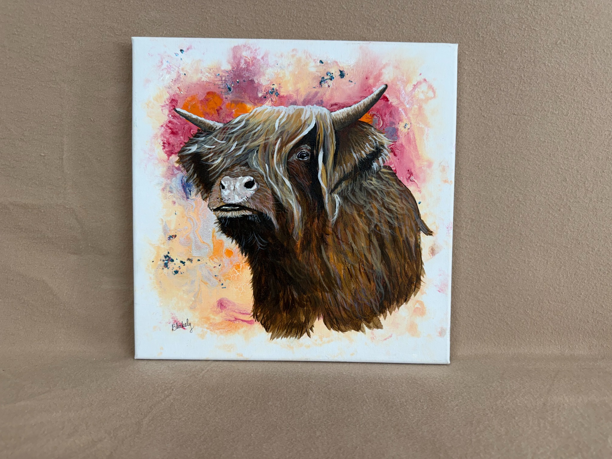 Highland Coo by Hope Blakely, 12 by 12 watercolor and acrylic painting of a shaggy brown Highland cow against pink and orange abstract colors.