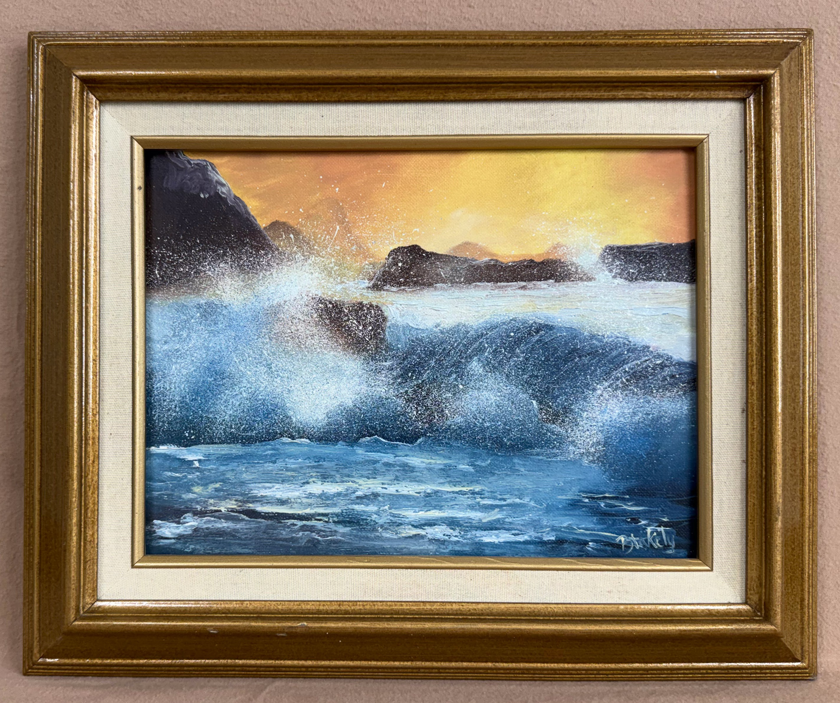 Original oil painting Arise by Hope Blakely, showing a powerful blue ocean wave crashing over dark coastal rocks beneath a glowing golden sunset.