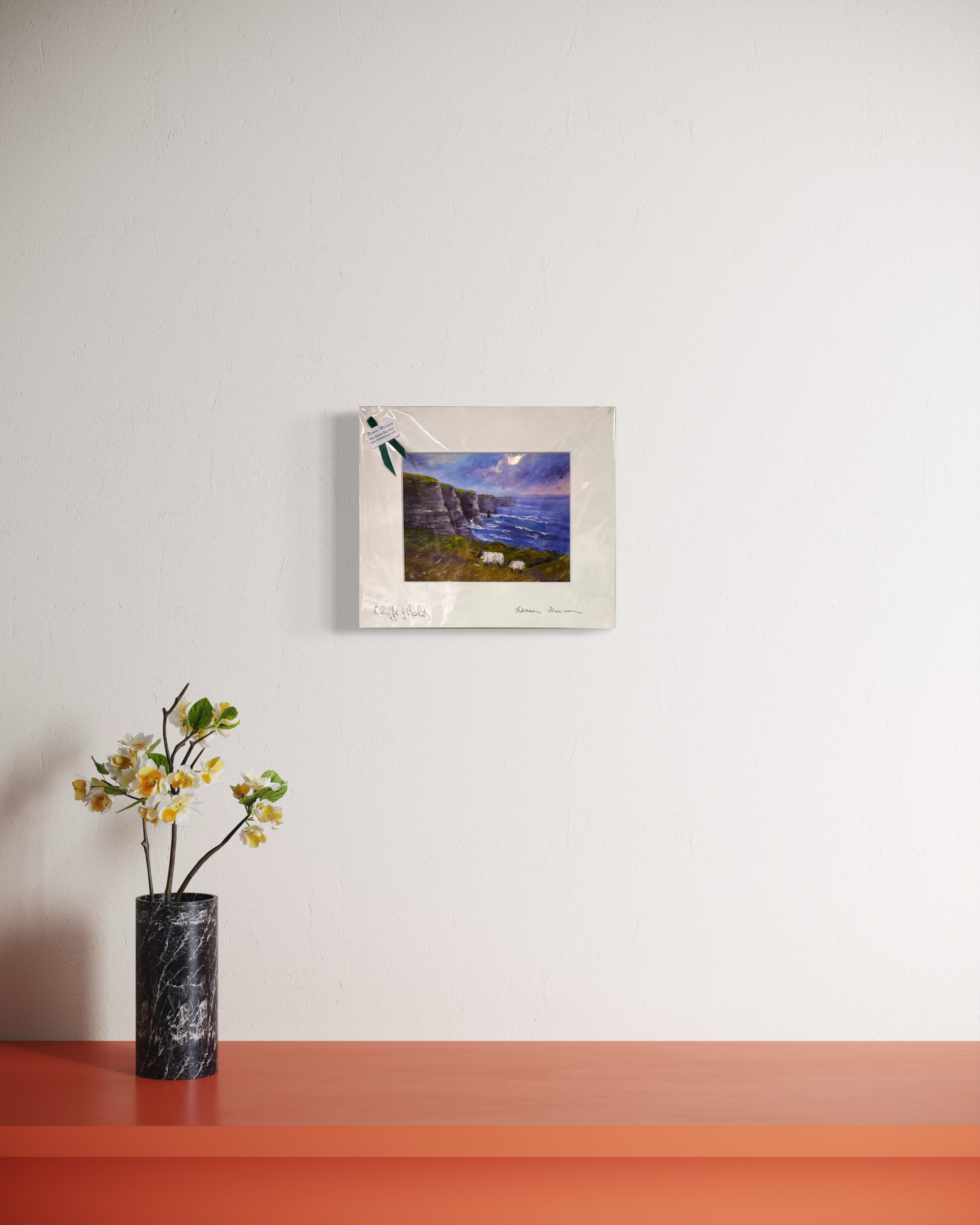 Cliffs of Moher matted painting displayed in a room above a red console with yellow flowers.