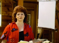 Diane André standing warmly beside a blank canvas outdoors, introducing a new painting lesson with her signature calm, encouraging presence.