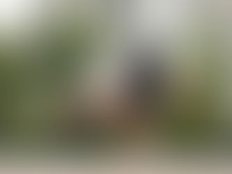 Man in athletic wear balances in yoga crow pose on a blue mat outdoors, with palms and buildings in the background. Determined focus.