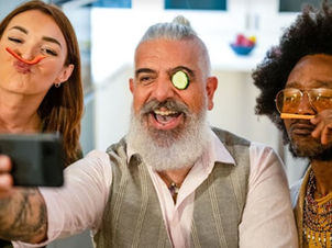 Three people joyfully take a selfie, each with a vegetable slice on their face. Bright kitchen background, playful mood.