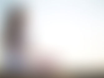 Woman in white meditating on a beach at sunset, seated cross-legged, hands in a mudra. Serene mood with soft, golden light.