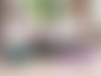 Woman in white activewear using a foam roller on a yoga mat in the living room. Pink shoes, teal dumbbells, and purple resistance band visible. Bright setting.