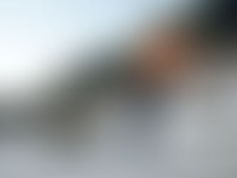 Shirtless man with mask pulling a large tire on a chain in a rocky, outdoor setting. Clouds of dust and trees in the background.