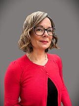Portrait of Kirsti Cox, founder of Kirsti Cox Advocacy, wearing glasses and a red cardigan against a neutral grey background