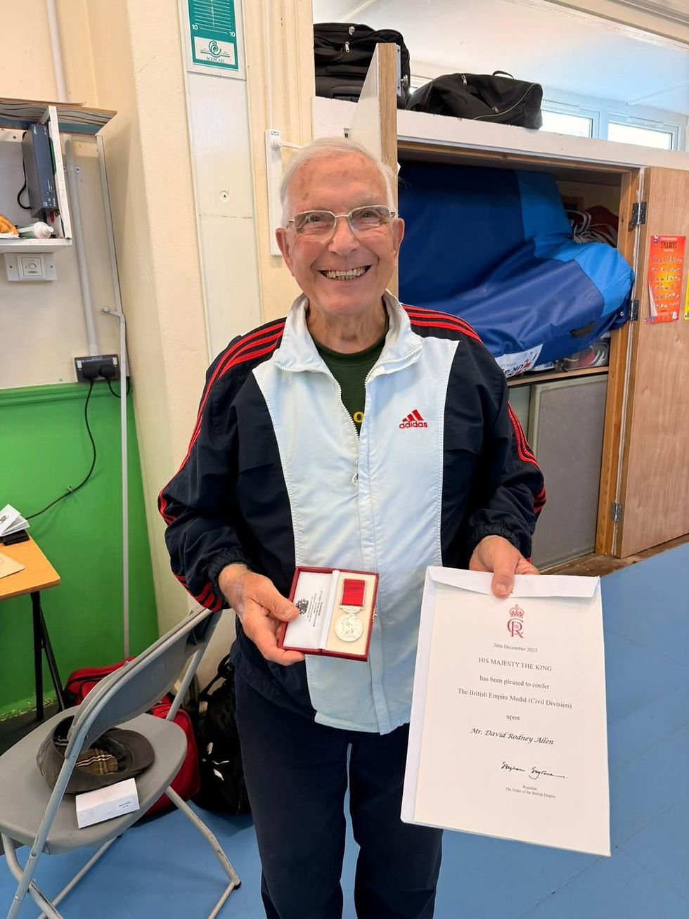 Eye-level view of Sir Dave standing proudly with the British Empire Medal in a community hall