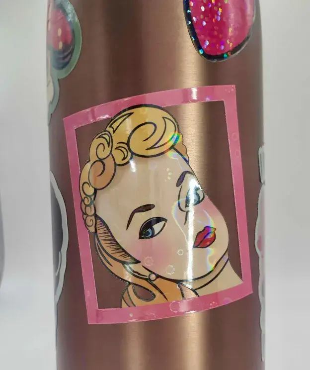 Thumbnail: Cartoon blonde doll head giving side-eye, surrounding by cut-out frame, sticker, stuck on a copper water bottle.