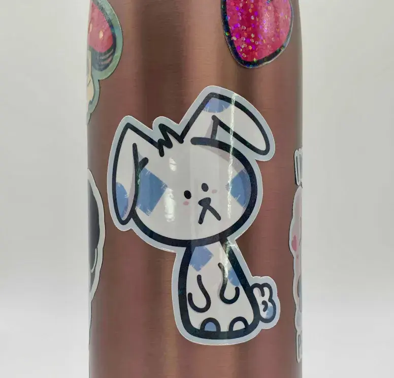 Thumbnail: Sad Blu Patchwork Bunny sticker, white with blue sewed patch spots, stuck on a copper water bottle.
