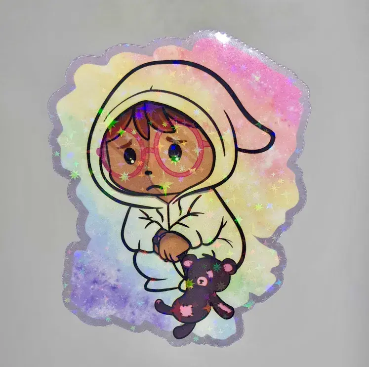 Thumbnail: Sad cartoon creature in a clear onesie holding teddy bear sticker, on plain background.