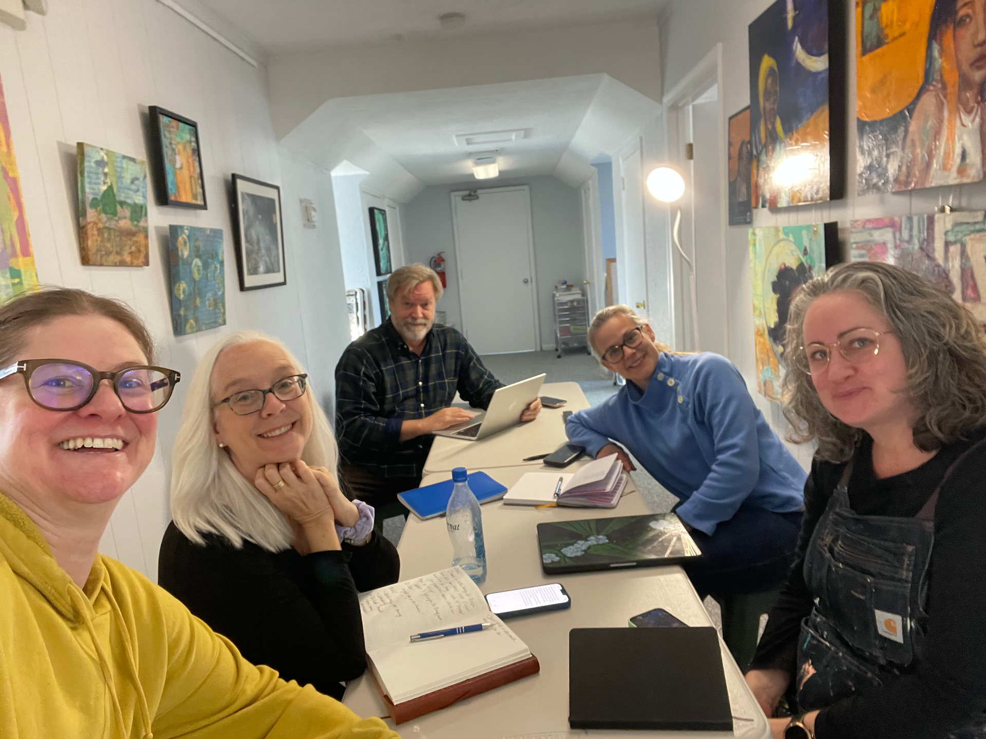 5 people sit at a table in the hallway at Idylwood Studios during a planning meeting. There is art on both walls.