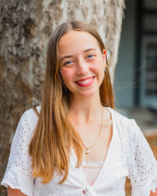 a white woman smiling gently while looking at the camera with a natural background