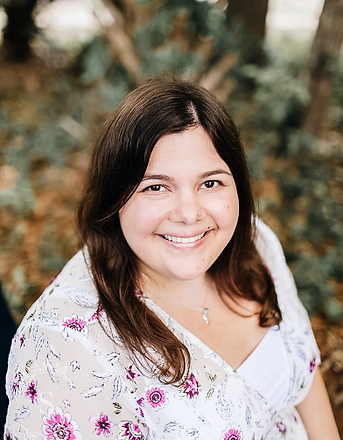 A picture of a white female looking up at the camera with an inviting smile in front of a soft natural background
