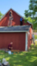 Professional painting crew working on the exterior of a red building using ladders and painting equipment.