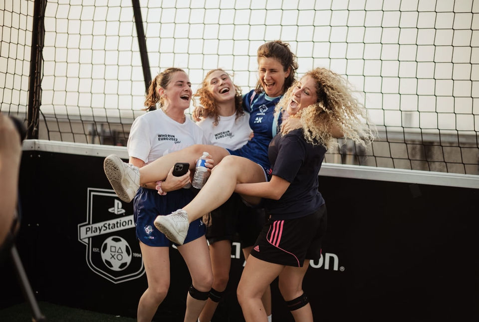 Image de 4 joueuses de foot féminin. Trois d'entre elles portent la quatrième. Elles sont heureuses de participer à un tournoi de foot dédié aux femmes à l'occasion de l'Euro de foot féminin 2022.