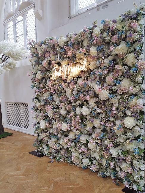 A mixed pastel flower wall with a Just Married neon sign attached to the front