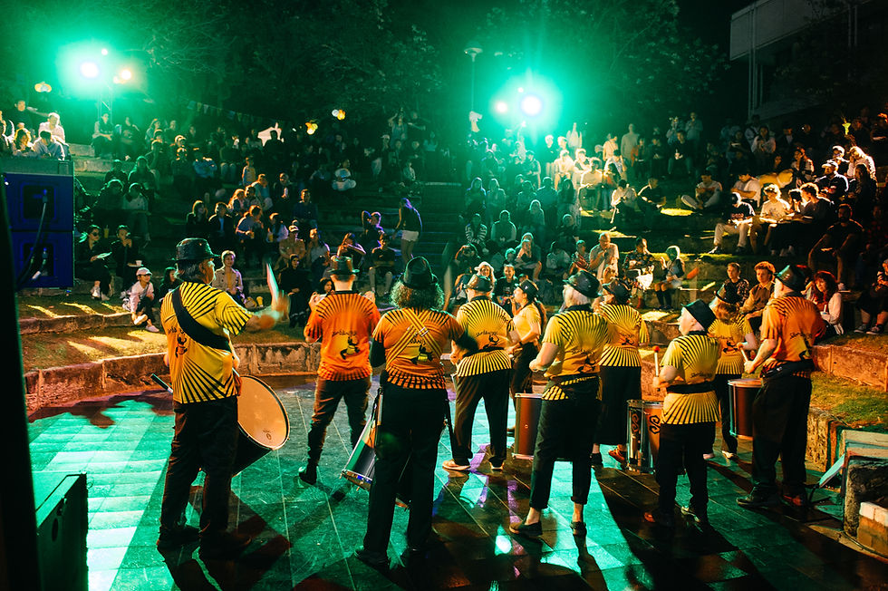 On stage, a group of drummers looking at the crowd. Image taken from behind the drummers.