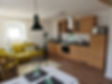 Helles Wohnzimmer mit offener Küche, Esstisch, Holzfußboden, dekoriert mit grünen Akzenten und moderner Beleuchtung.